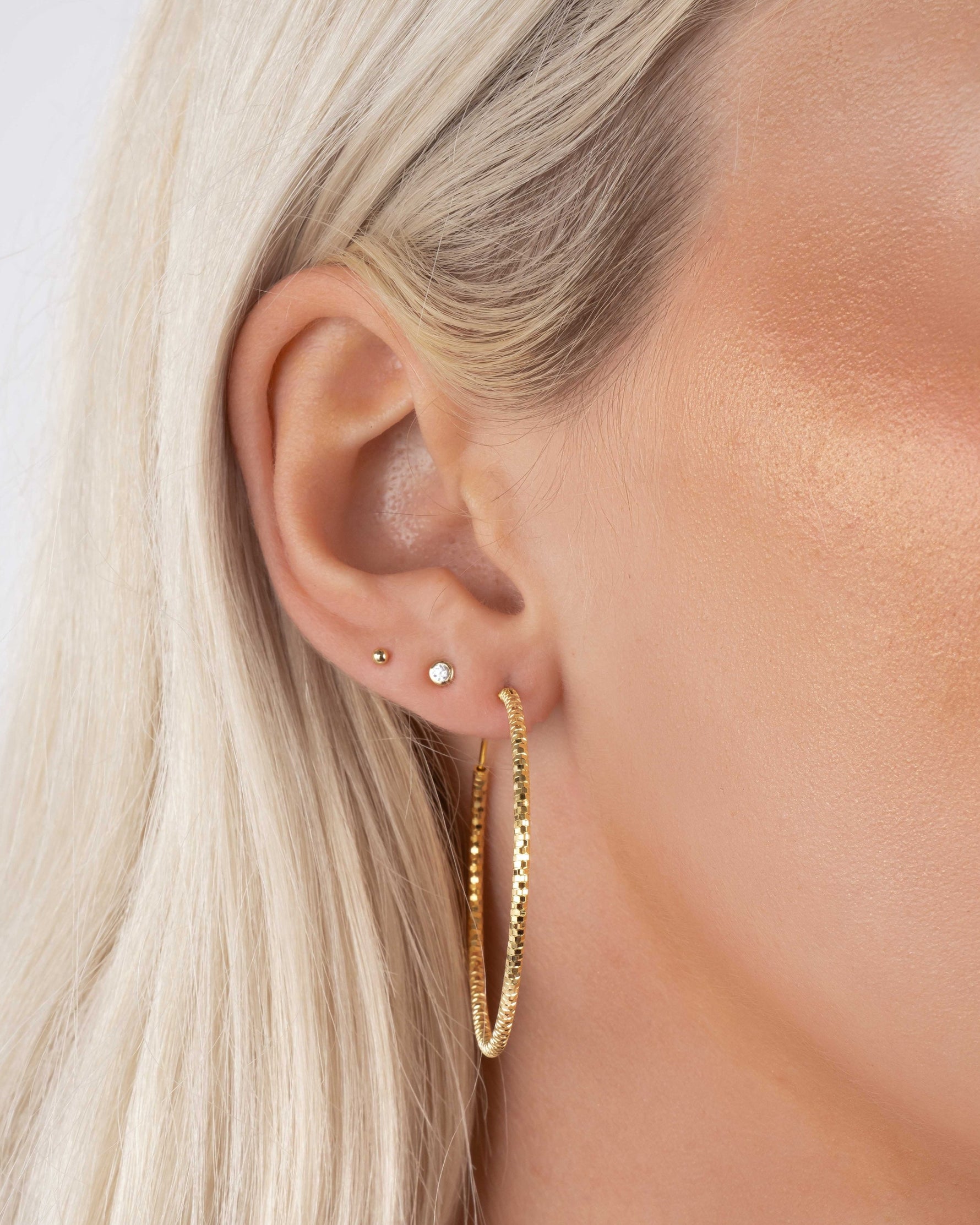 Gold 40mm hoop earrings on model, lightweight statement hoops paired with subtle stud earrings.
