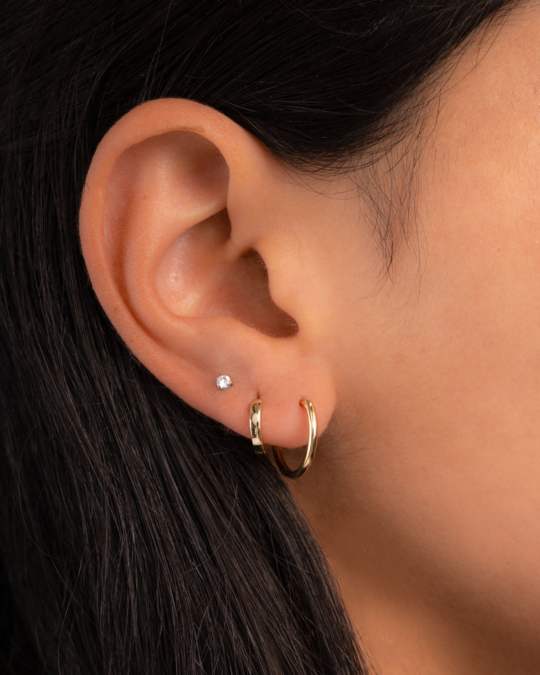 Model wearing gold earrings featuring a minimalist hoop earring, huggie earrings, and solitaire studs