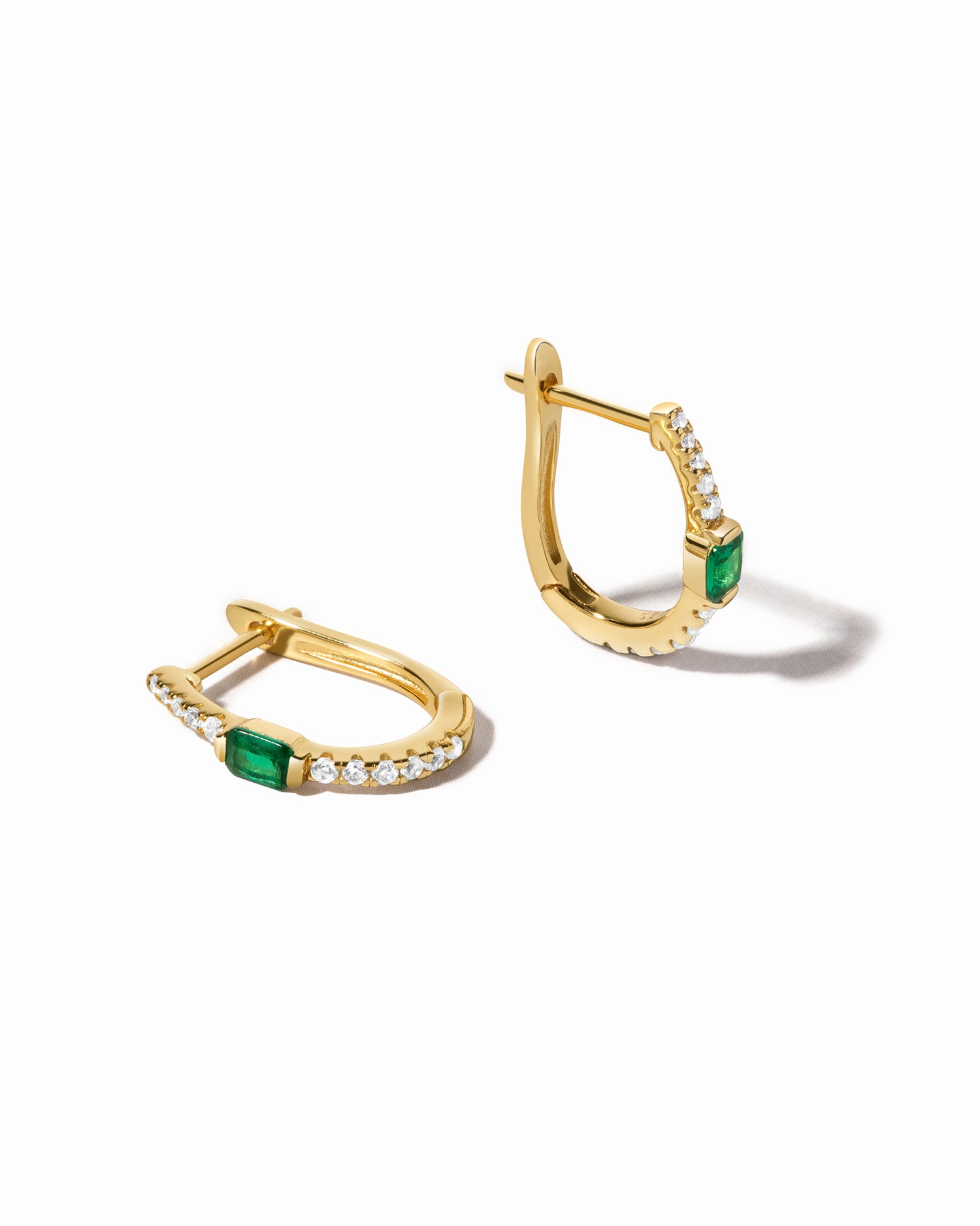 A pair of gold hoop earrings with emerald stones and diamond details, displayed against a white background.