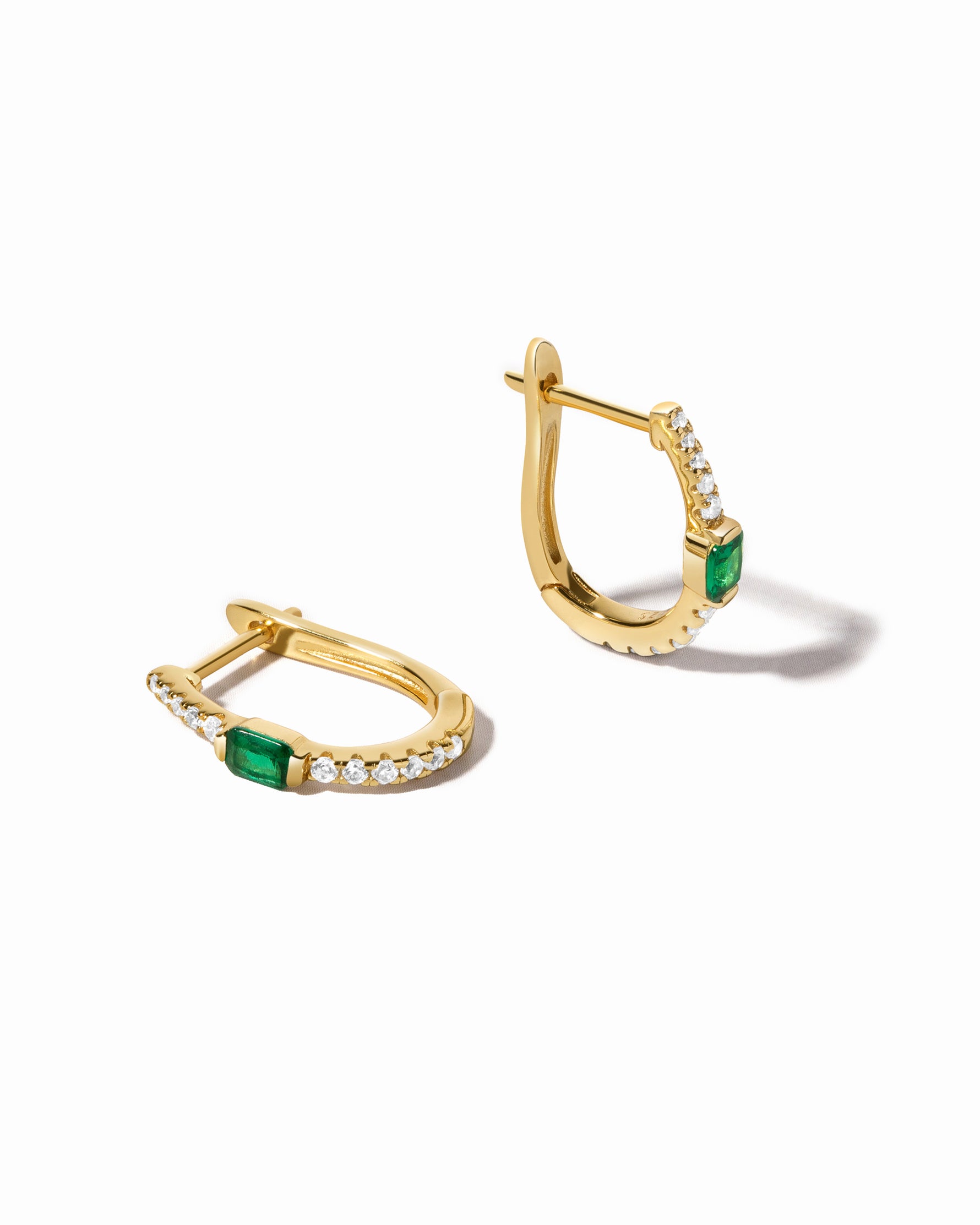 A pair of gold hoop earrings with emerald stones and diamond details, displayed against a white background.
