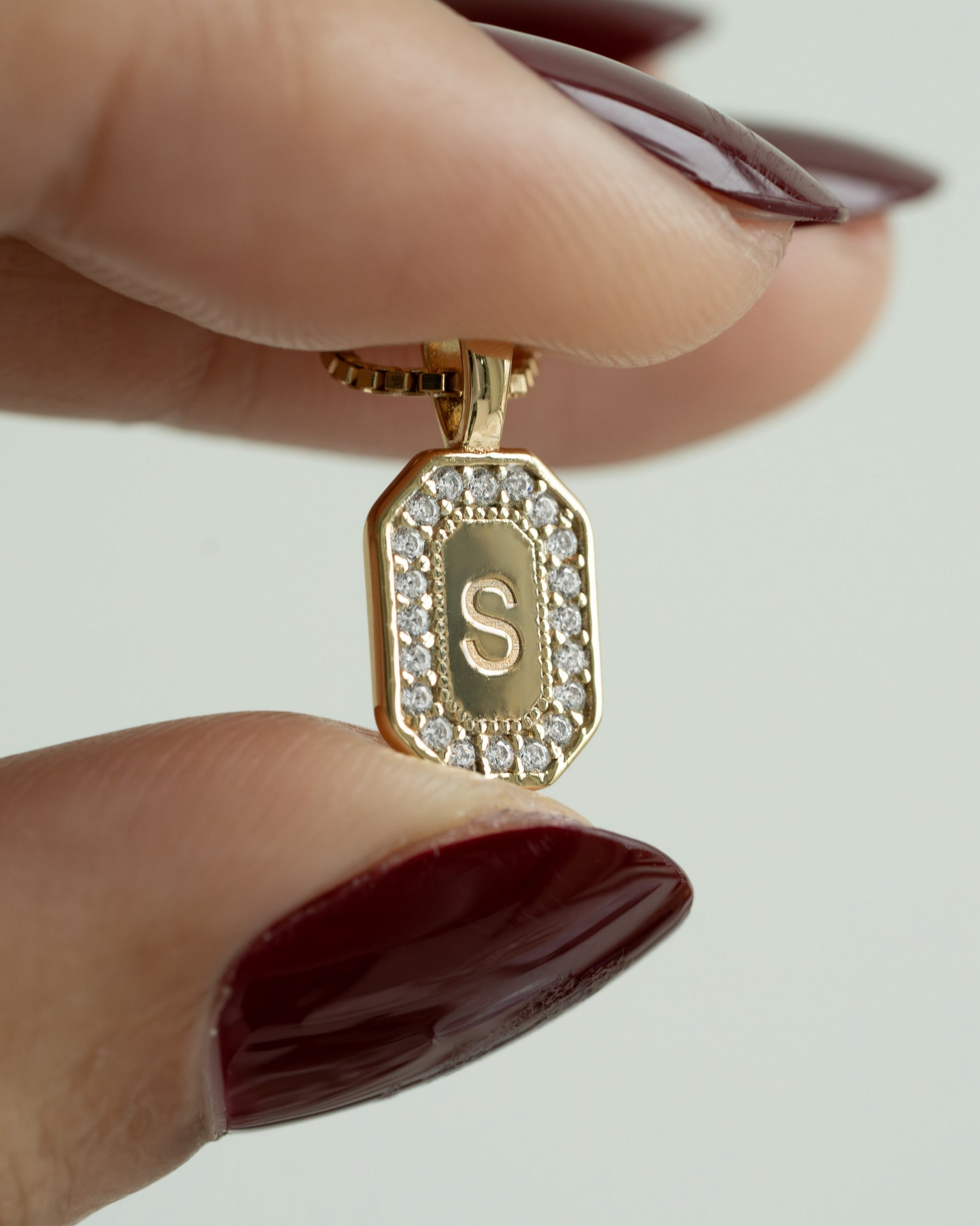 Gold personalized initial necklace with a pendant featuring the letter 'S' held between two fingers.