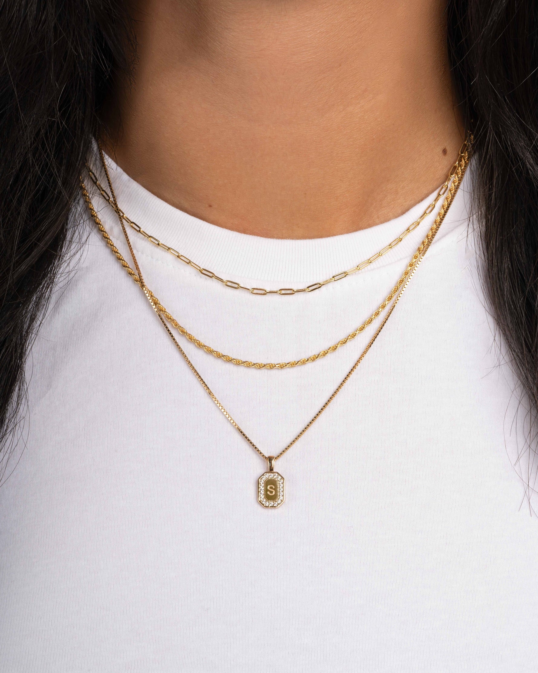 Model wearing gold chain necklaces featuring a small paperclip chain necklace, a rope chain necklace, and a dainty gold engraved initial necklace