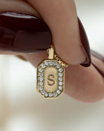Closeup image of model holding a personalized gift featuring a custom pendant initial necklace with a "S" initial, in between two fingers 