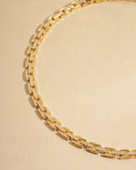 Gold statement jewelry featuring a choker necklace on a beige background