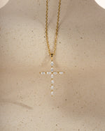 Gold cross pendant layering necklace on a beige background