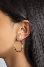 Model wearing gold hoops, with a marquise cut diamond earring in her second and a small stud earring also marquise cut in her third 