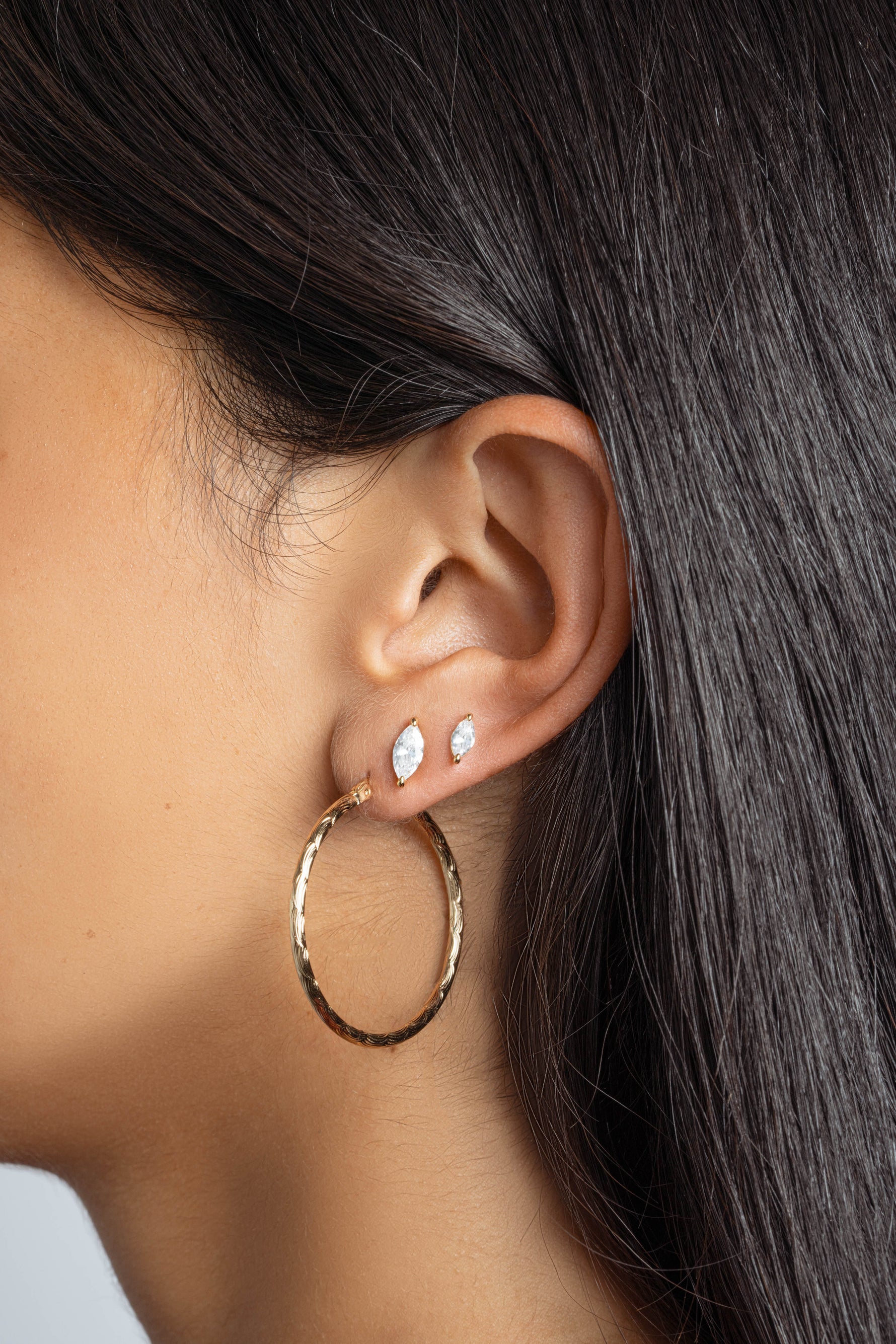 Model wearing gold hoops, with a marquise cut diamond earring in her second and a small stud earring also marquise cut in her third 