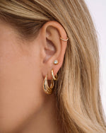 Model wearing chunky hoops, simple huggie earrings, and a diamond stud earring