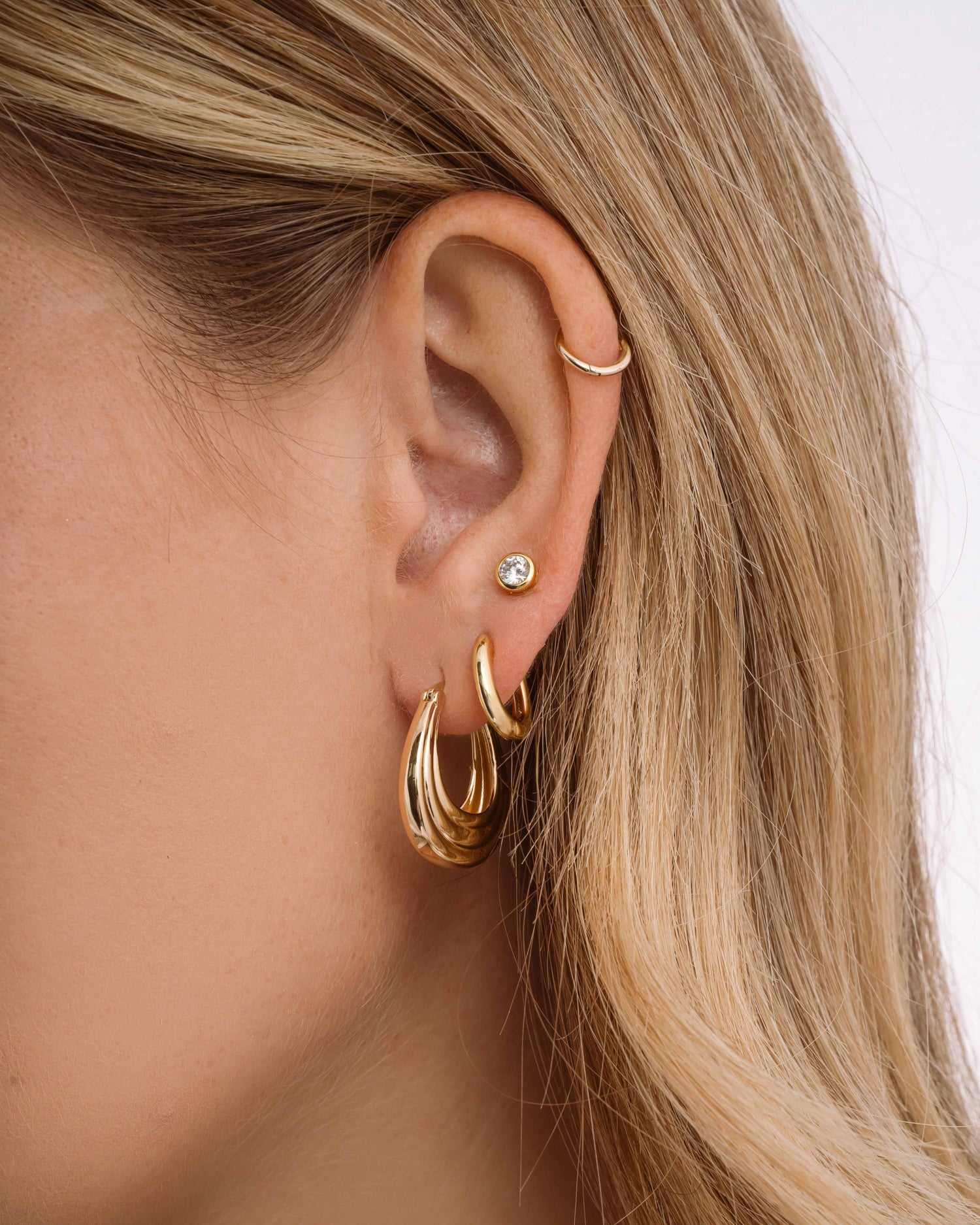 Model wearing chunky hoops, simple huggie earrings, and a diamond stud earring