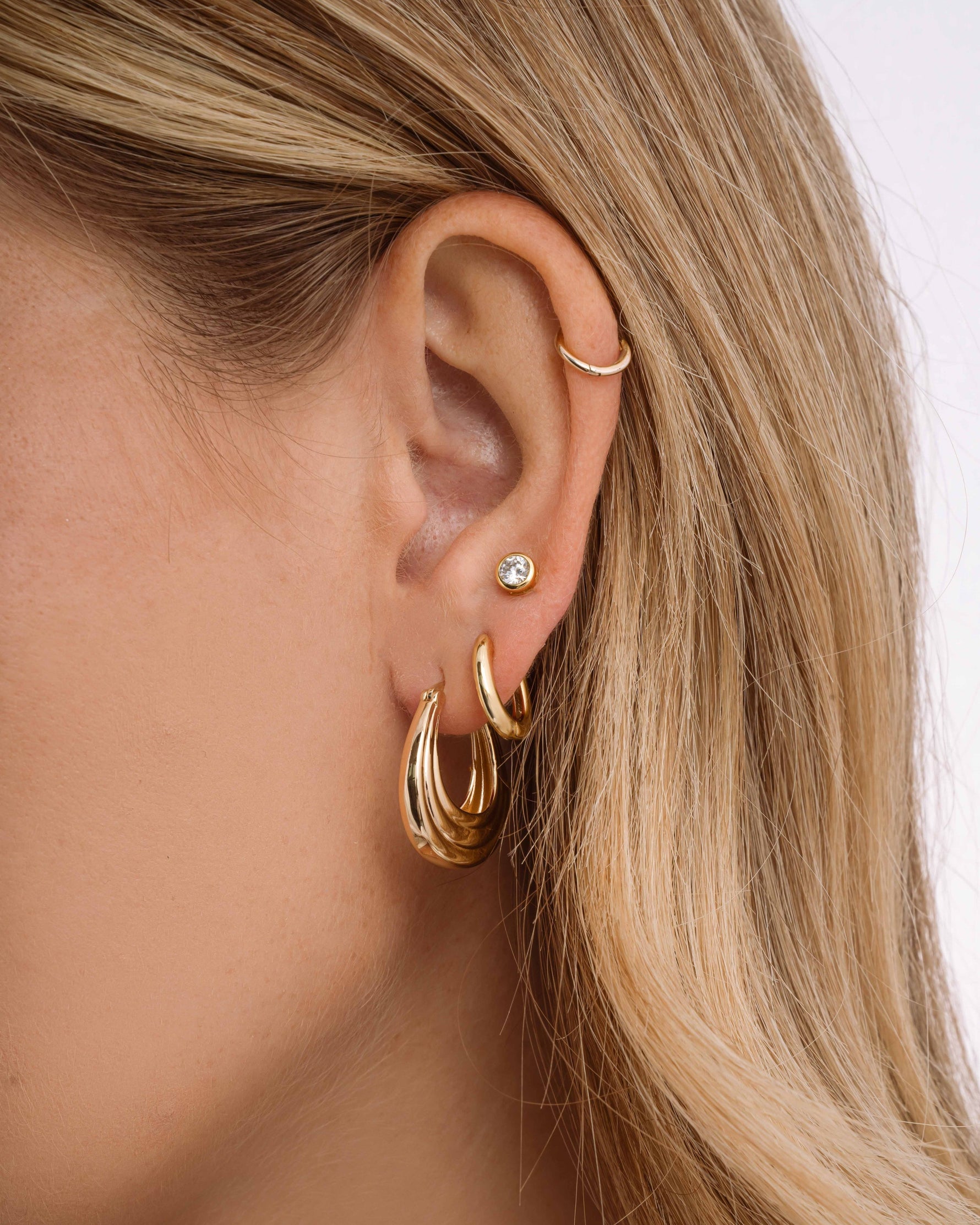 Model wearing chunky hoops, simple huggie earrings, and a diamond stud earring