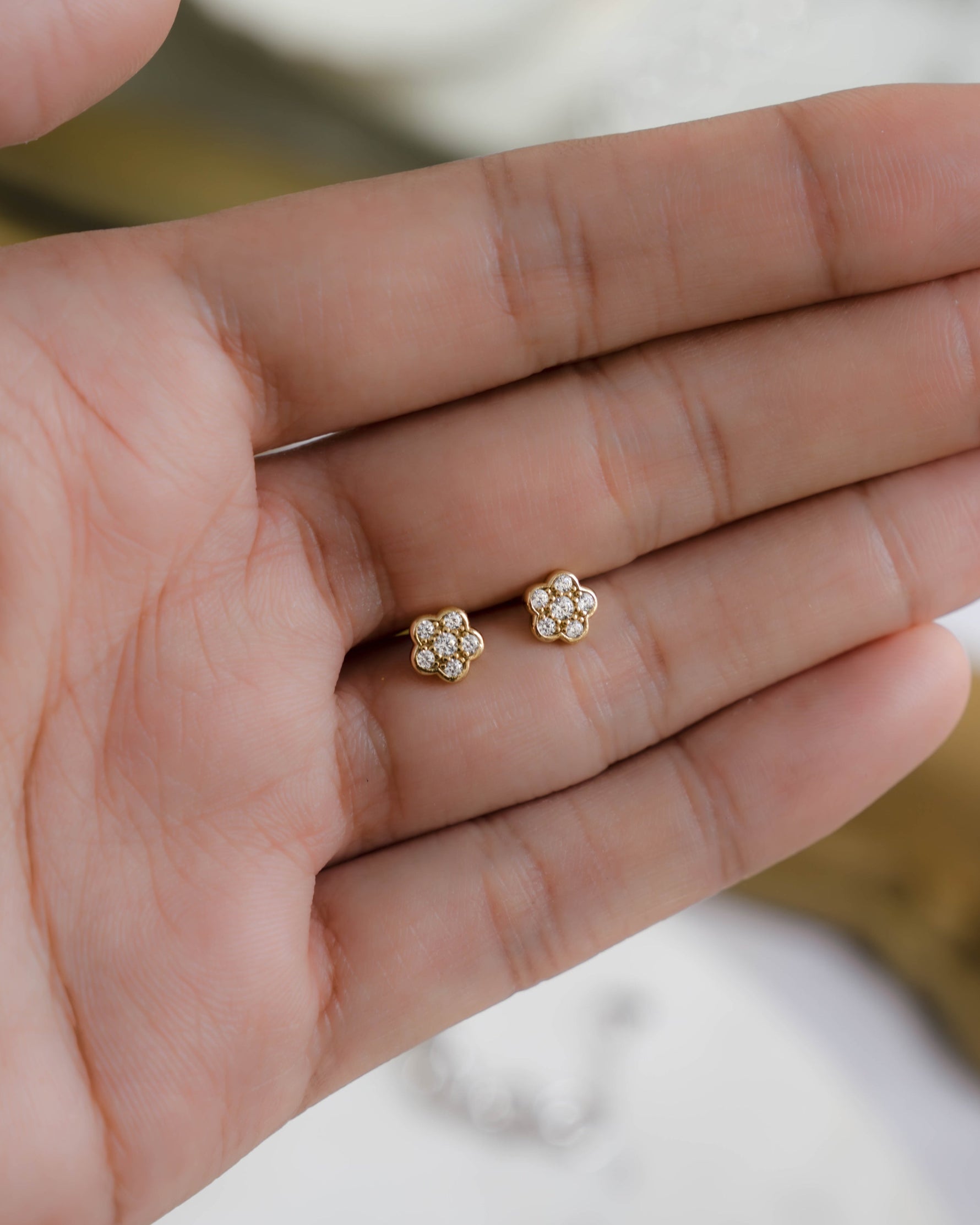 Closeup image of the palm of a hand showcasing dainty diamond flower earrings 