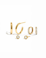 Gold hoop earrings, gold huggie hoops, and diamond stud earrings on a white background 