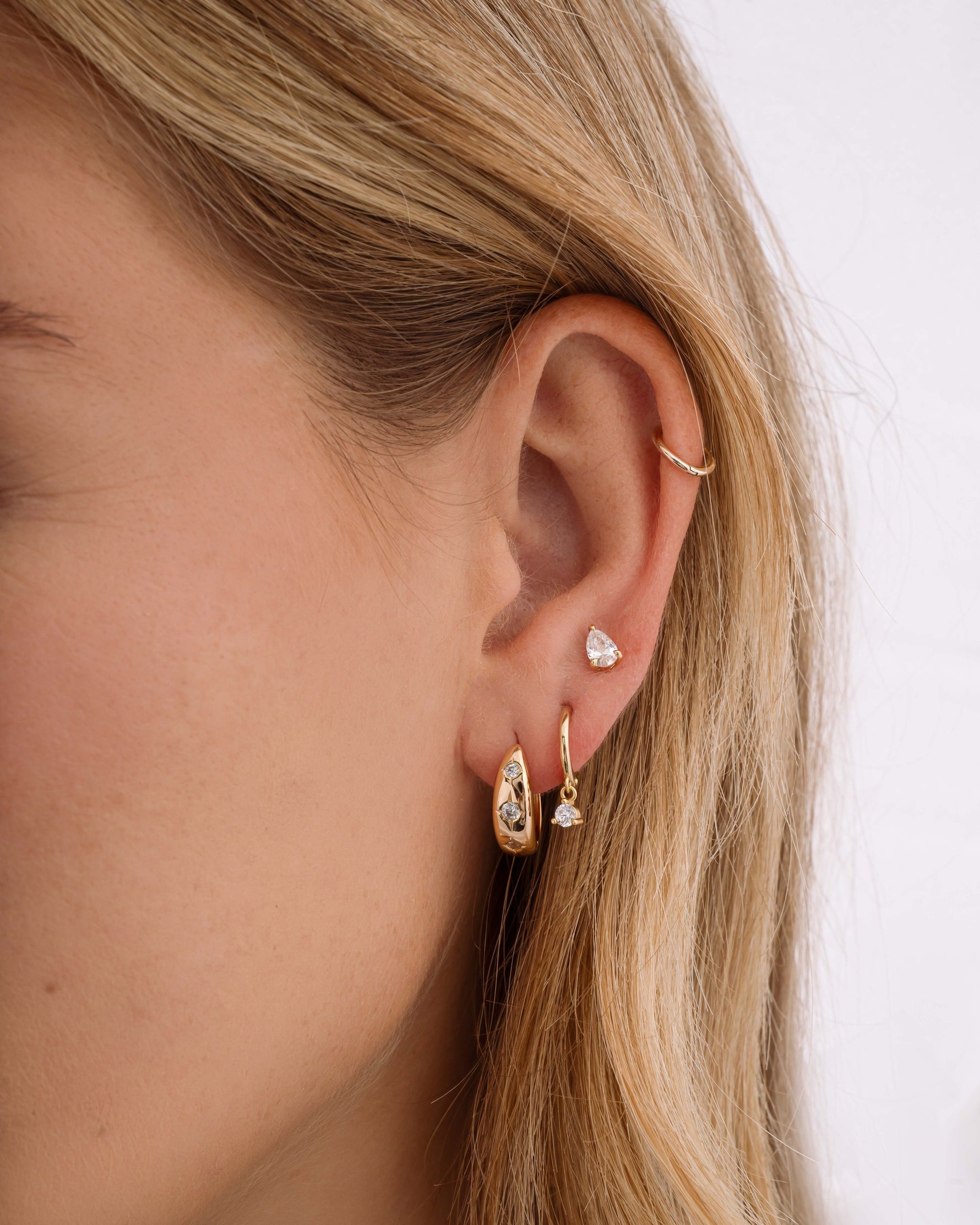Close-up of a person's ear wearing gold hoop earrings, dainty huggie hoop earrings, and a small stud earring  