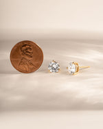 Gold stud earrings being compared to the size of a penny