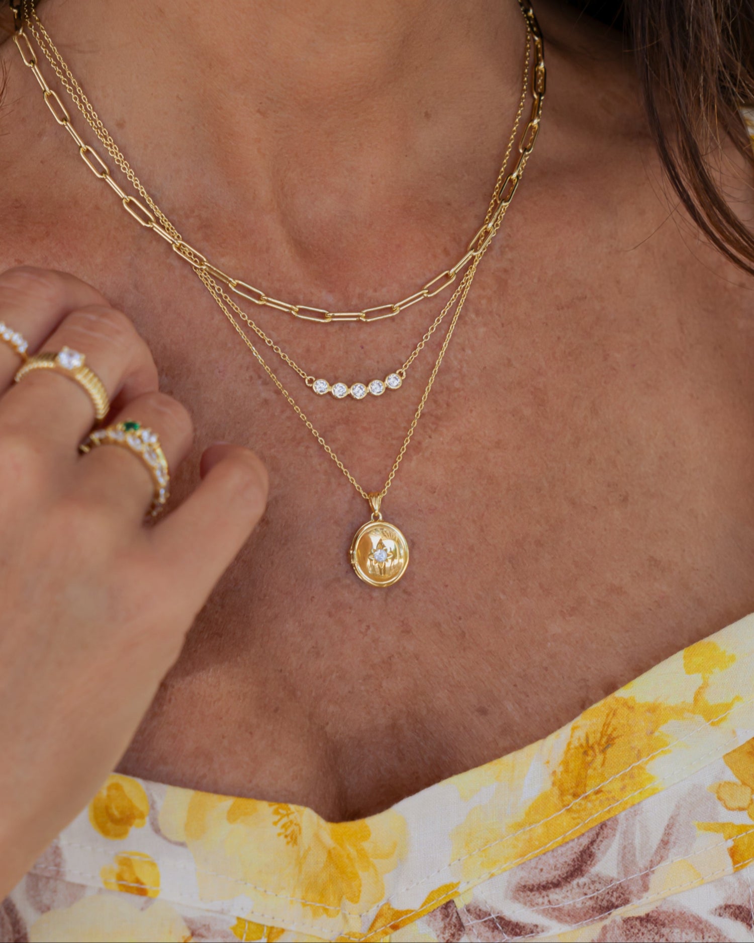 Woman wearing a gold 5 stone necklace, paired with a paperclip necklace and gold pendant necklace 