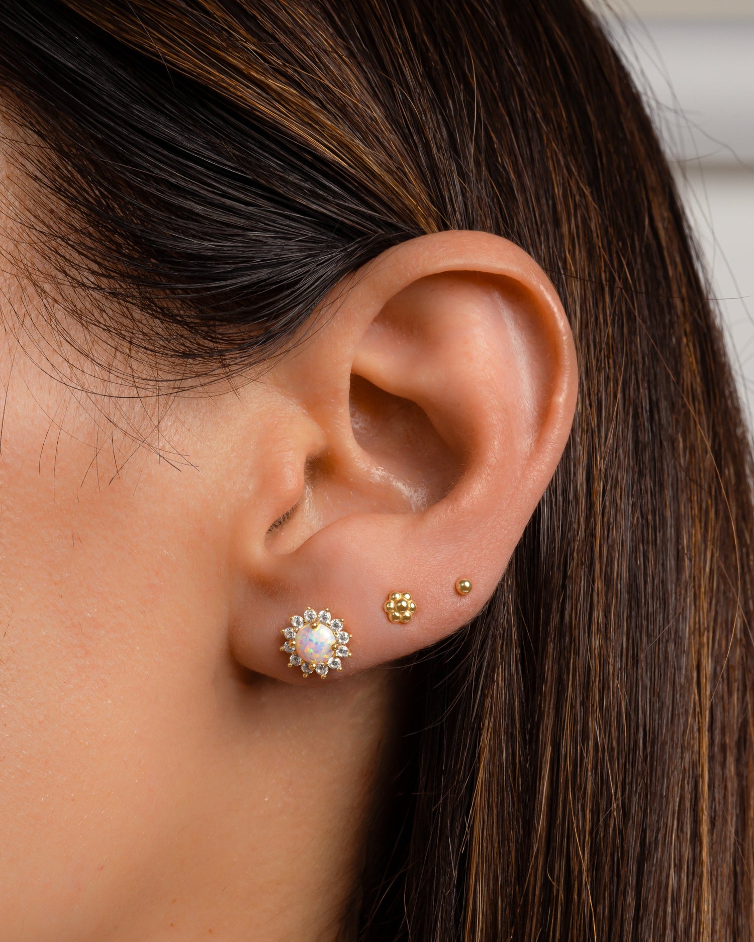 Close-up of an ear wearing gold and opal stud earrings with a blurred background
