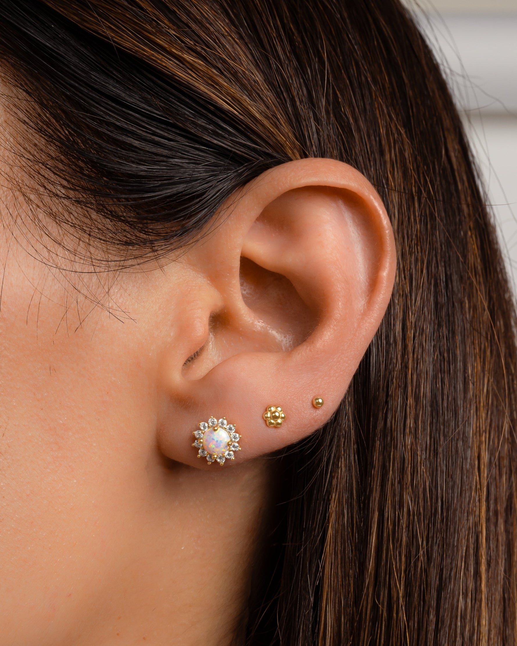 Close-up of an ear wearing gold and opal stud earrings with a blurred background