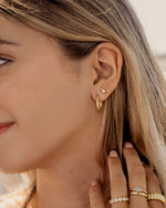 Close-up of a woman wearing gold hoop earrings and stackable rings with a blurred background
