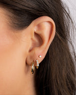 Close-up of a models ear wearing gold oval hoop earrings, a cubic zirconia hoop earring, and a bezel stud earring 