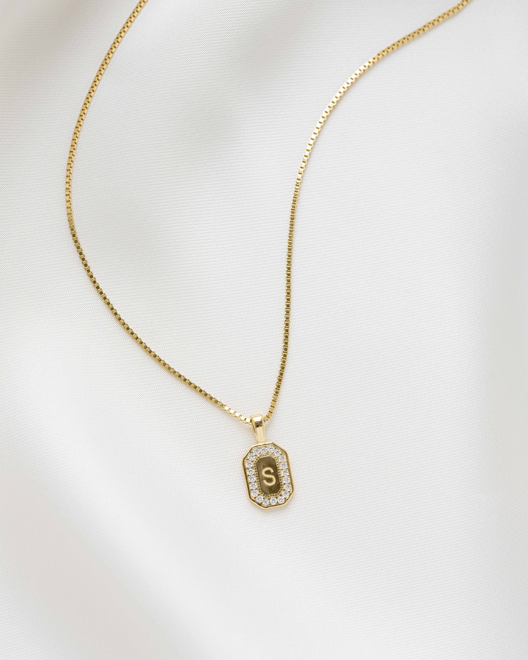 Gold diamond necklace with a custom diamond pendant of an "S" initial on a white background