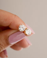 Diamond stud earrings held between fingers against a neutral background