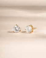 Gold solitaire stud earrings on a white background