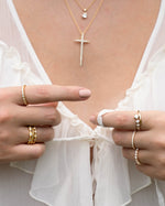 Model wearing gold vintage jewelry featuring a diamond pendant necklace, a cross necklace, gold stackable rings, and a diamond ring set