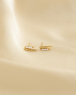 Closeup image of gold dainty stud earrings on beige background