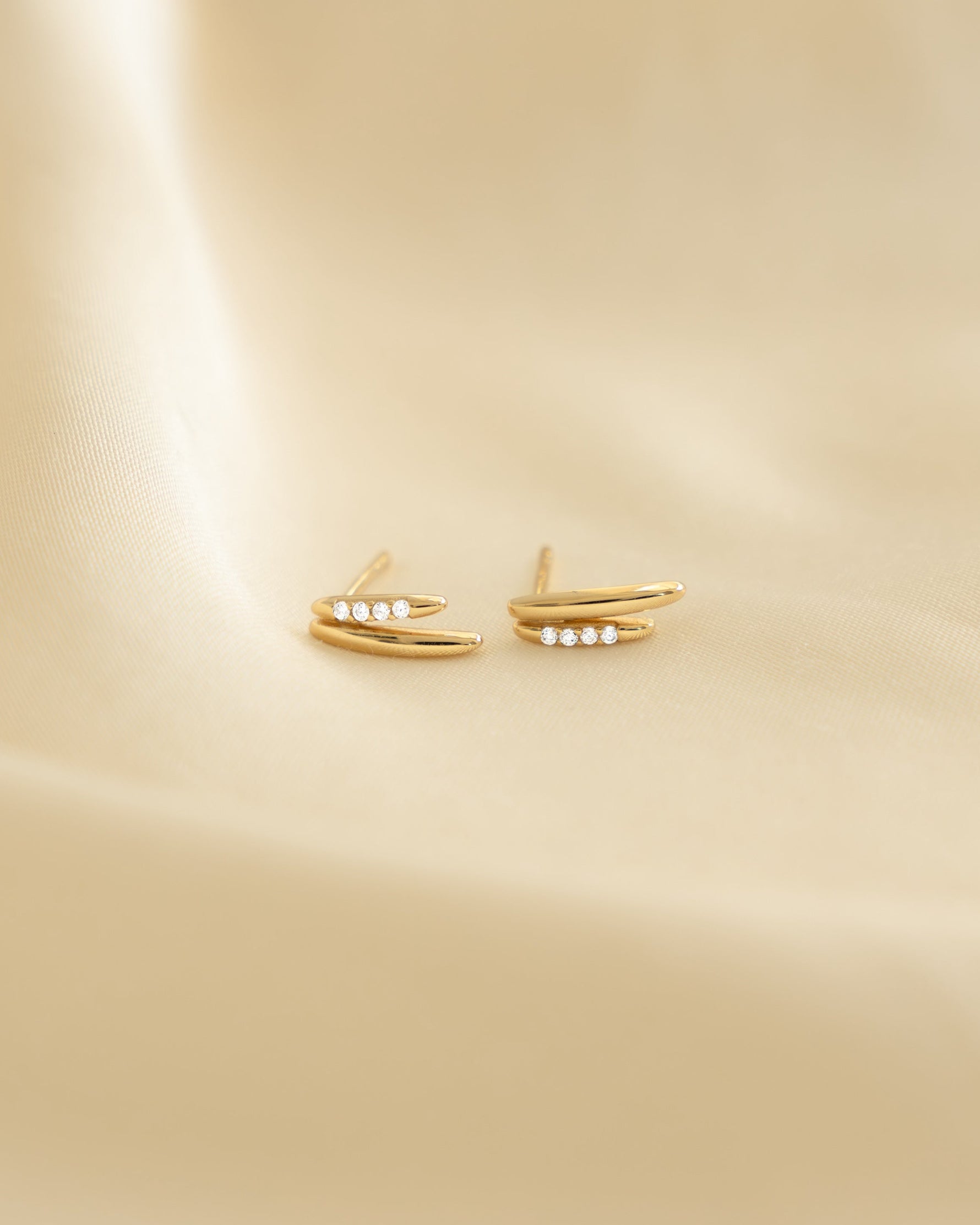 Closeup image of gold dainty stud earrings on beige background