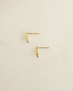 Gold tiny earrings lying on their side on a plain surface