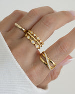 Model wearing golds featuring a gold stackable ring set, a statement ring, and a eternity band