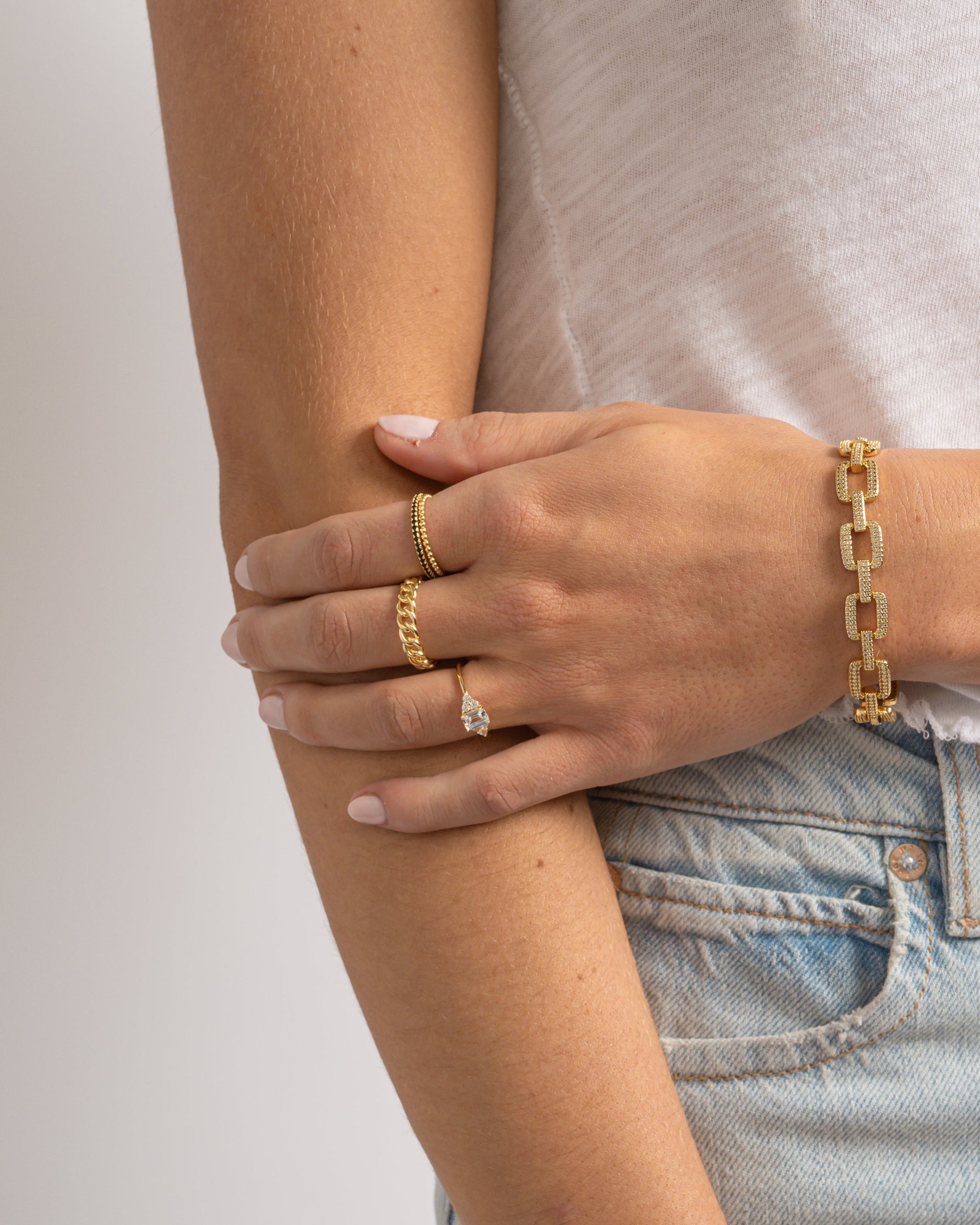 models wearing gold bracelets and a ring on a plain background