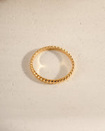 Gold simple stacking ring on a textured beige surface
