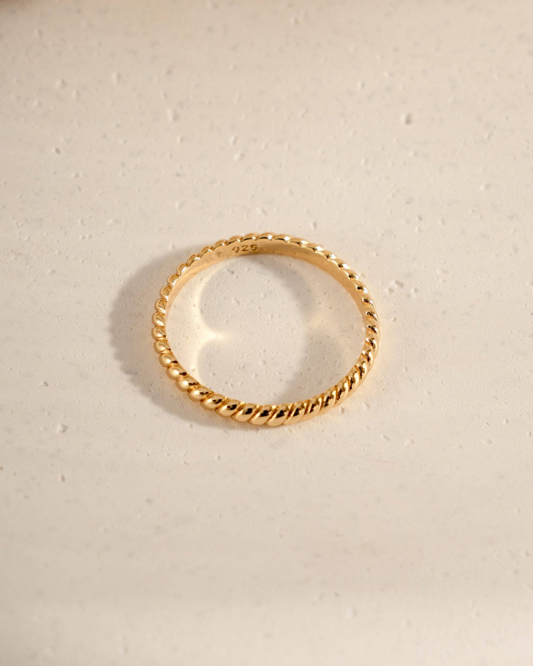 Gold simple stacking ring on a textured beige surface