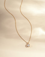 Gold necklace with a small round  diamond pendant on a beige background