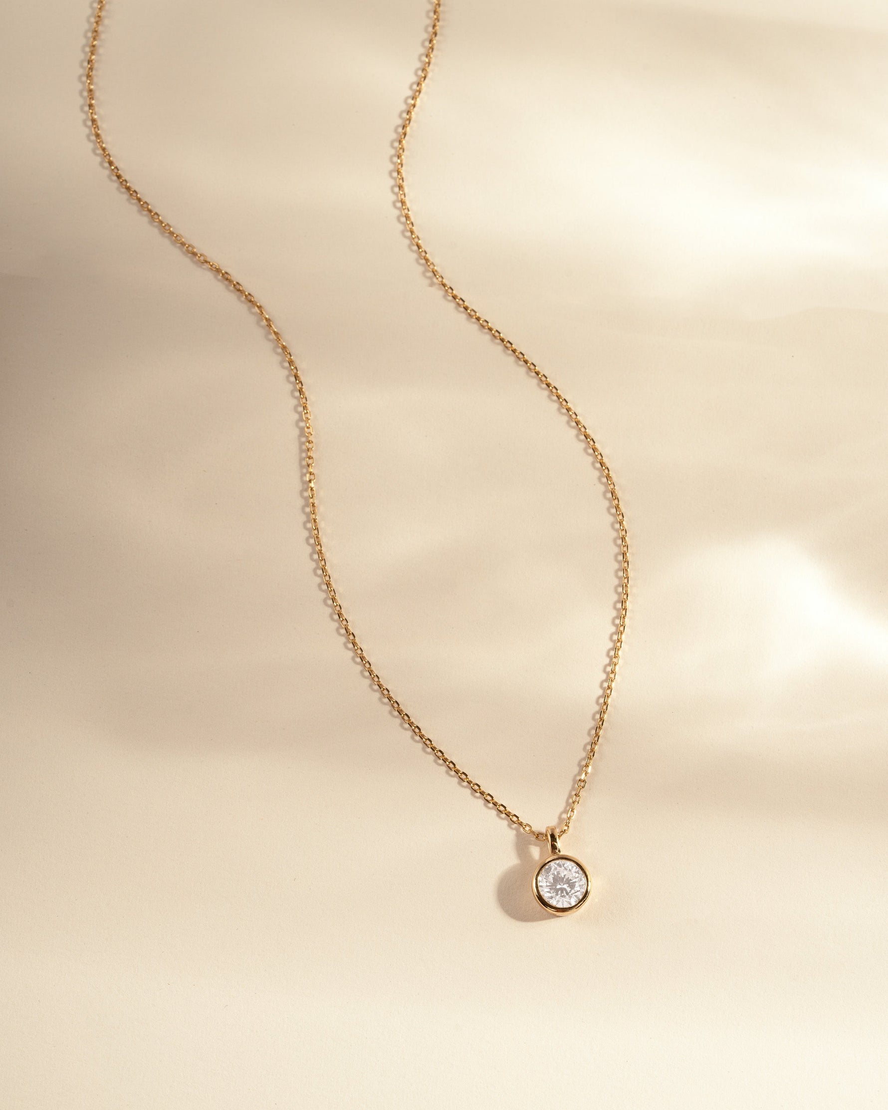 Gold necklace with a small round  diamond pendant on a beige background
