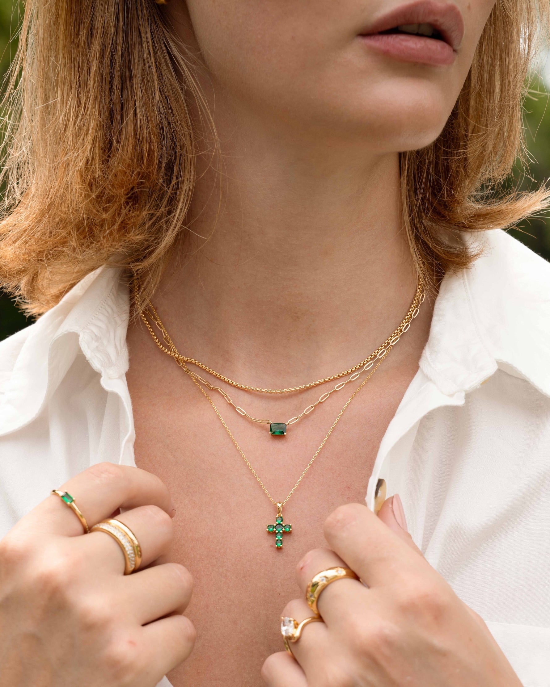 Model wearing gold layering necklaces with emerald pendants, featuring a simple box chain necklace and gold plated stackable rings