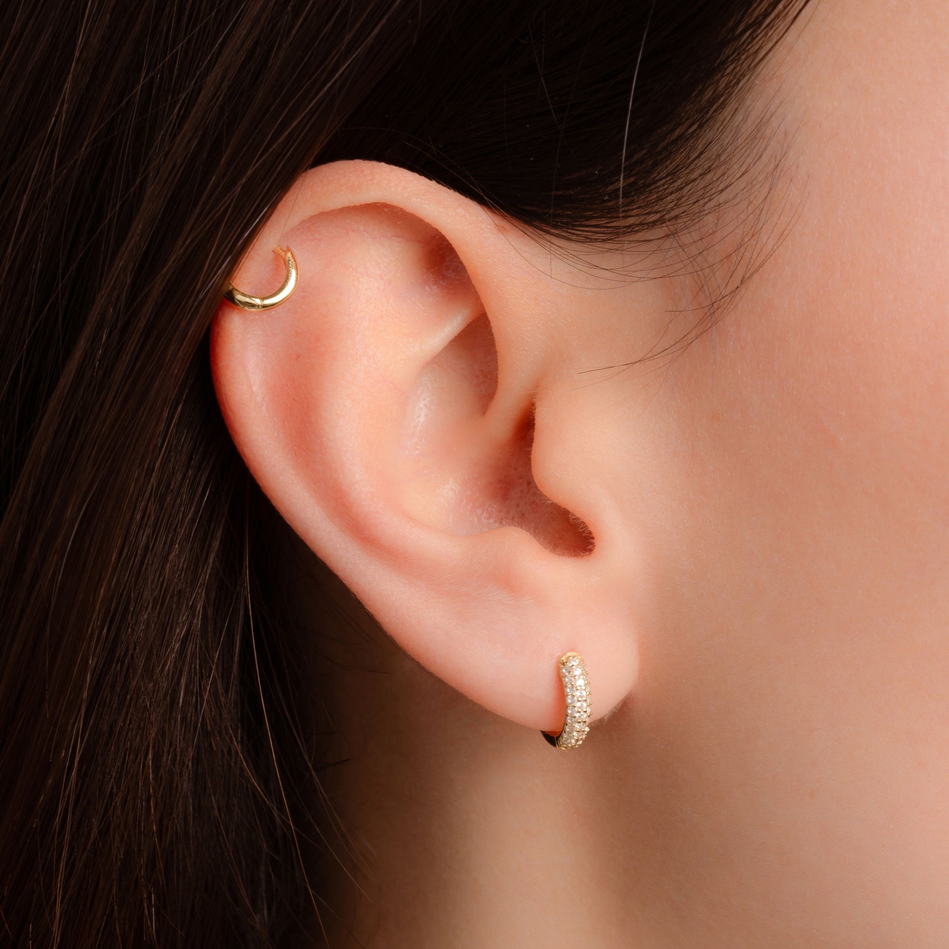 model wearing small hoop earrings featuring a gold huggie hoop dainty earring and a small gold hoop in the cartilage
