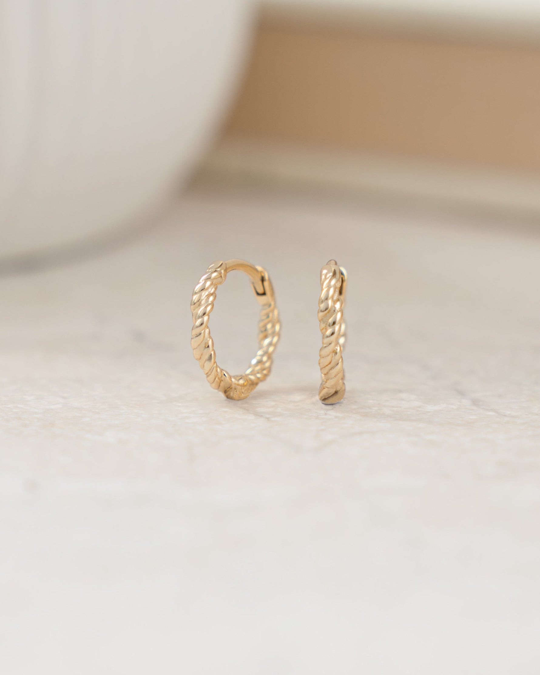 Mini gold hoops featuring a twisted hoop earring design 