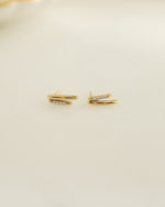Dainty gold studs with a geometric earring design on a beige surface