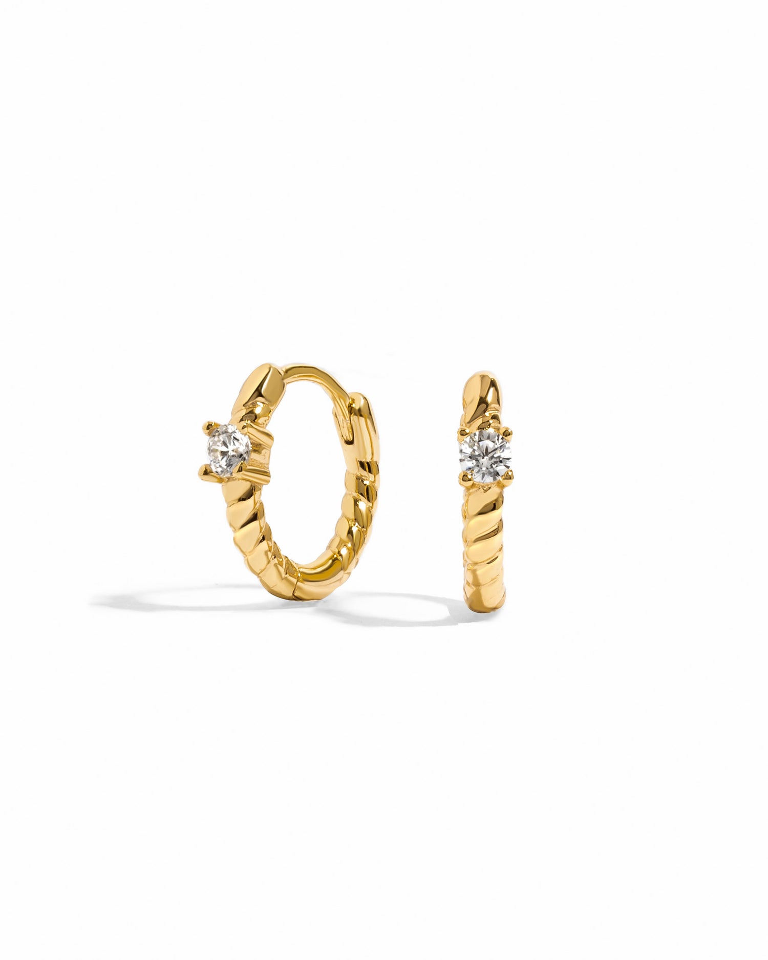 Gold spiral huggie hoop earrings with a small diamond on a white background