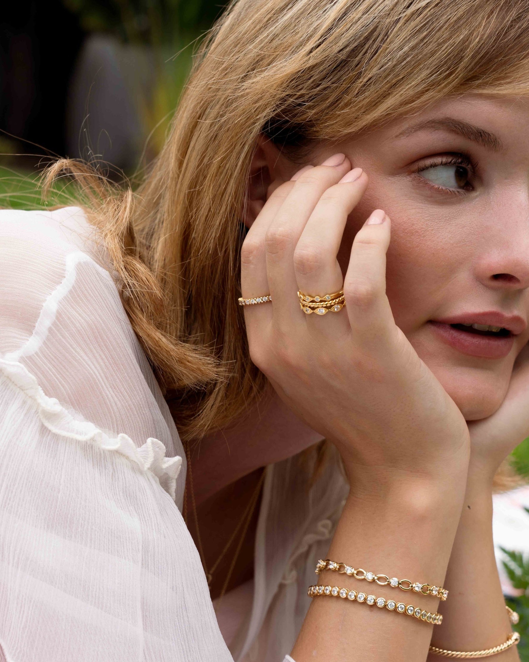Model wearing delicate gold jewelry featuring a vintage ring set with diamond rings, a dainty stackable ring, and dainty diamond tennis bracelets
