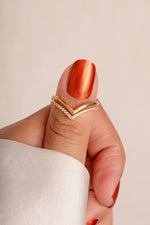 Model holding a minimalist gold chevron ring set on their thumb. 