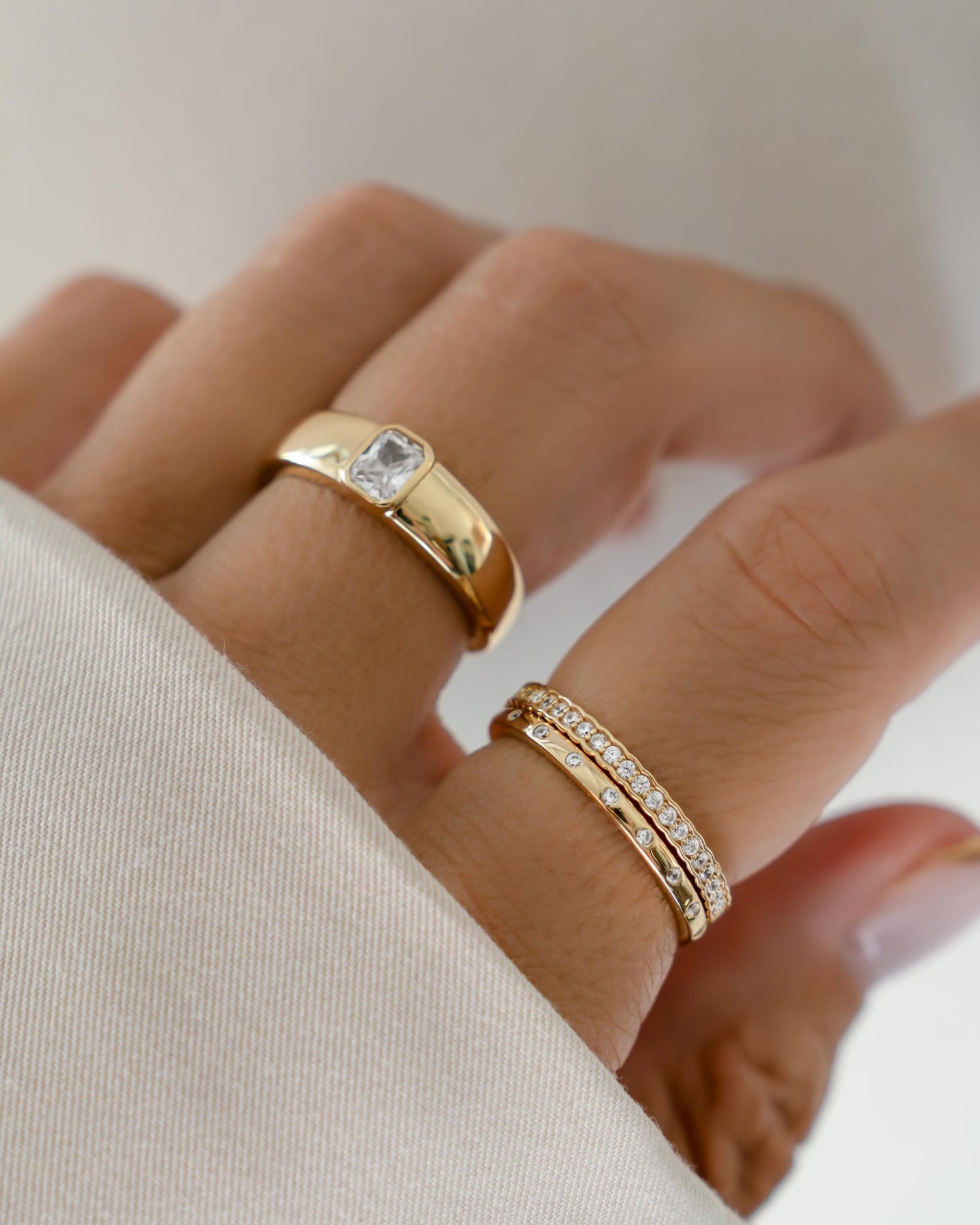 Models hand wearing baguette dome ring, a cz eternity band, and a multi stone diamond ring 
