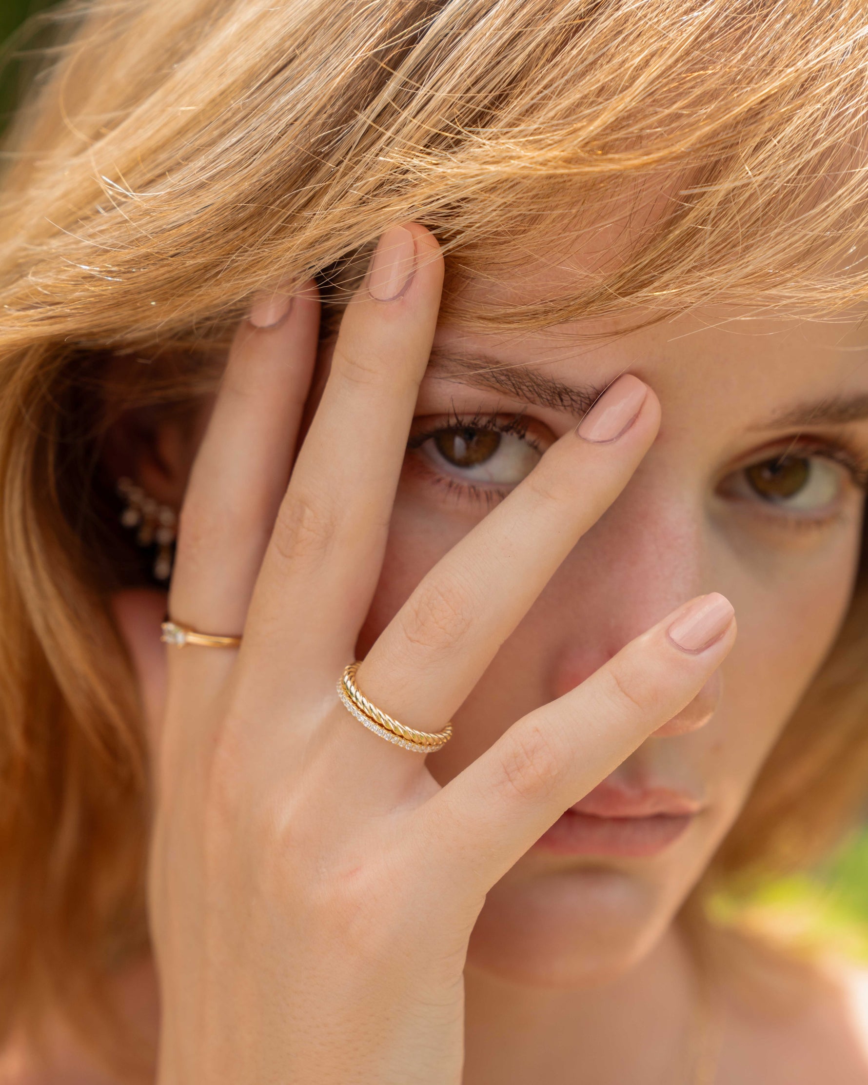 Woman with hand on face, wearing stacking gold rings, outdoors
