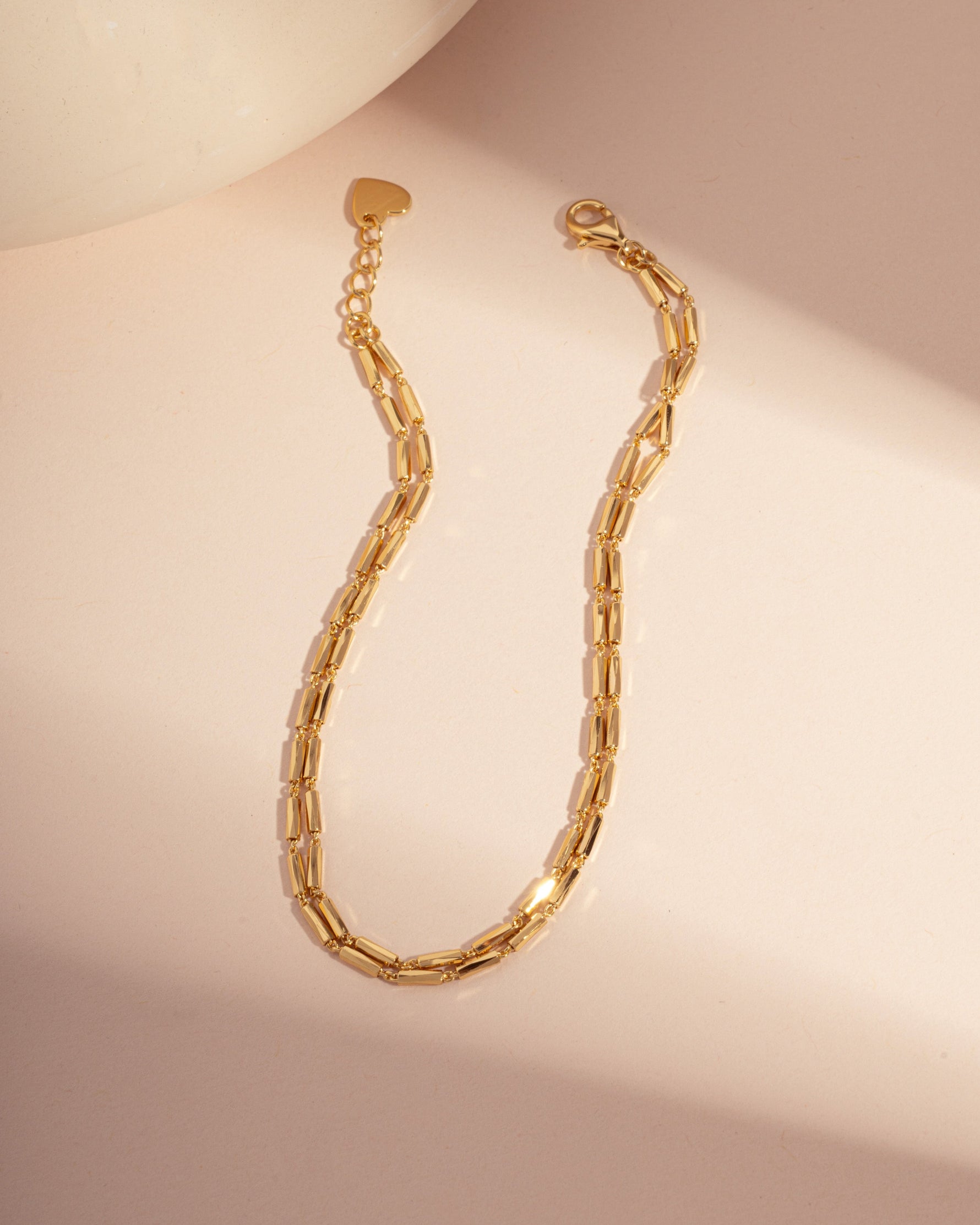 Gold minimalist bracelet set with a beaded bracelet design on a pink background