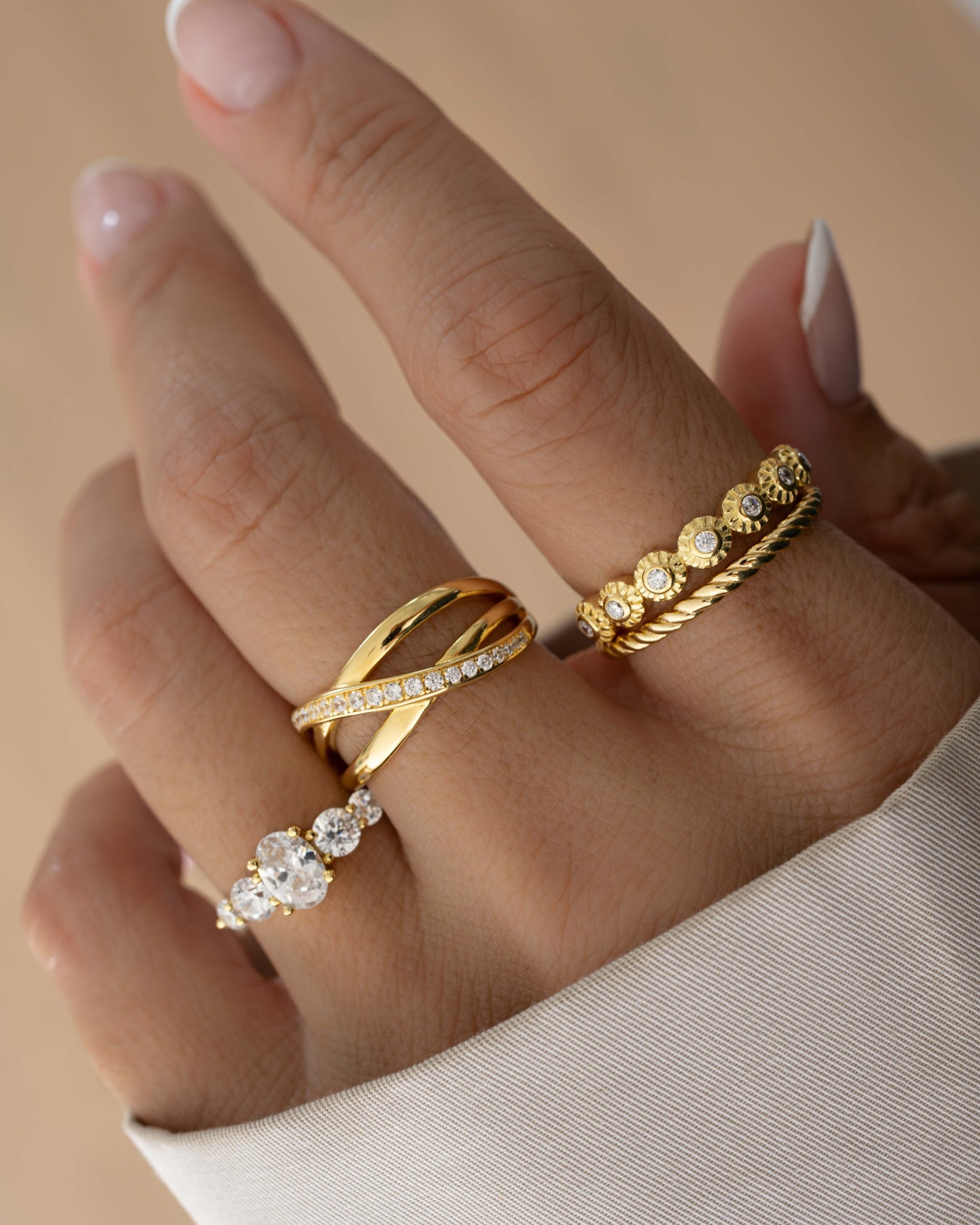 closeup image gold double band stackable ring with cubic zirconia diamonds going across, a bezeled stacking ring, a rope ring, and a oval diamond stacking ring