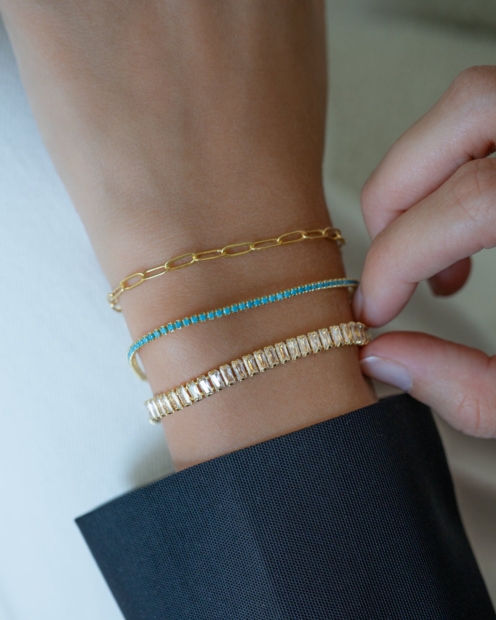 Model wearing gold small paperclip bracelet, turquoise tennis bracelet, and a baguette gold tennis bracelet, perfect for stacking bracelets