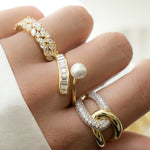 Model wearing gold stacking rings, one gold diamond cluster ring, one diamond baguette ring with freshwater pearl, and one cz statement ring