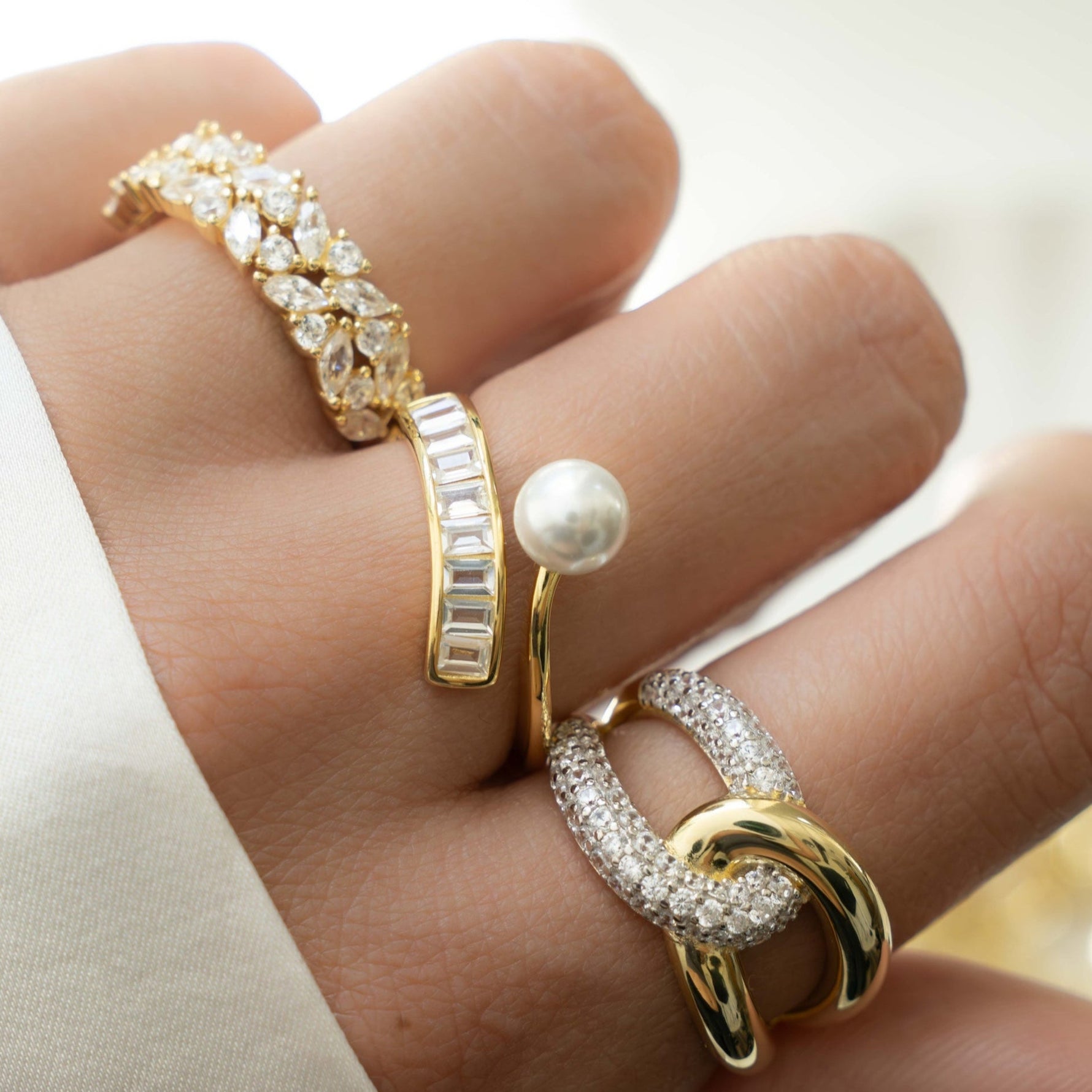 Model wearing gold stacking rings, one gold diamond cluster ring, one diamond baguette ring with freshwater pearl, and one cz statement ring
